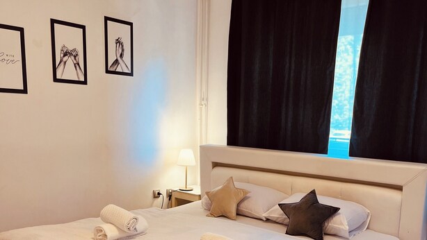 A neatly made bed with towels, a bedside lamp, and a window with curtains. - İstanbul Apartment (Belgrade)
