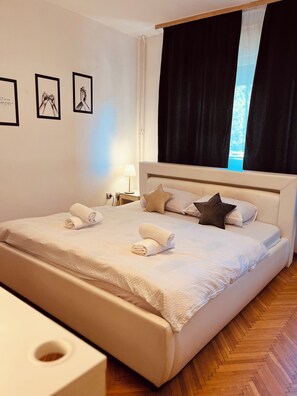 Una cama bien hecha con toallas, una lámpara de noche y una ventana con cortinas.