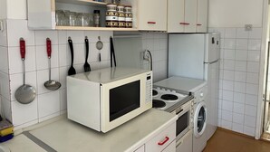 A compact kitchen with white cabinets, a microwave, a stove, and a washing machine. - İstanbul Apartment (Belgrade)