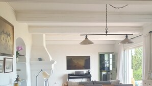 Tilava olohuone, jossa on ruokapöytä, tuoleja ja televisio. Taustalla on keittiö, jossa on kaappeja ja ikkuna.