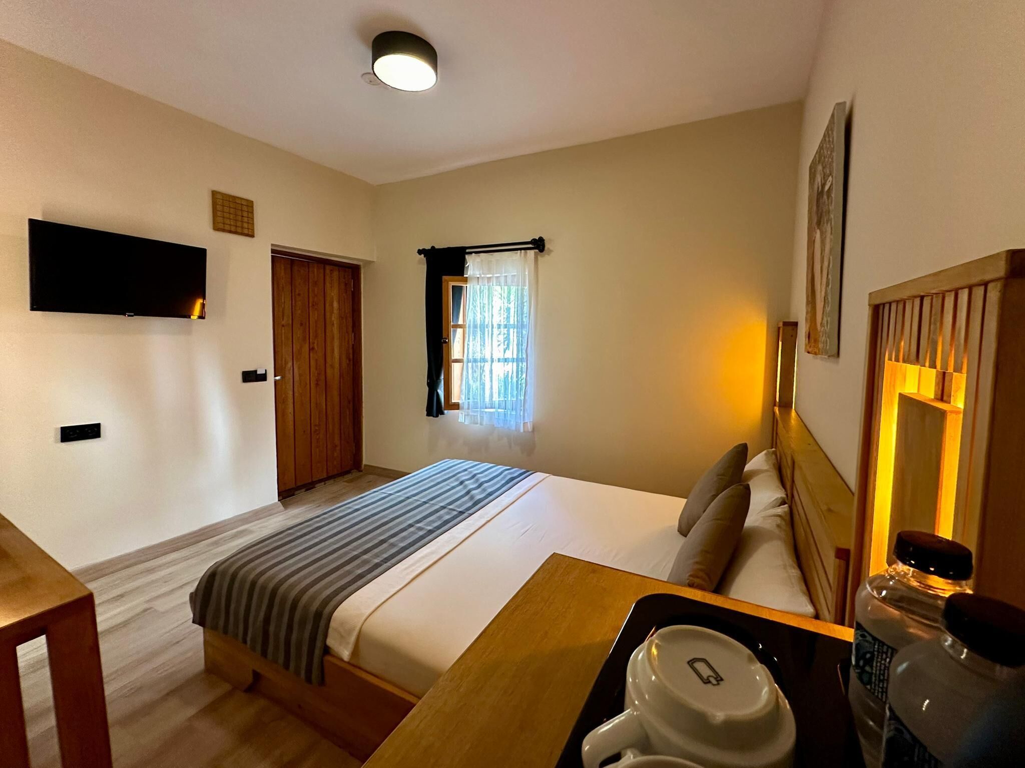 Habitación de hotel con cama, escritorio, silla, televisor, armario y ventana con cortinas.