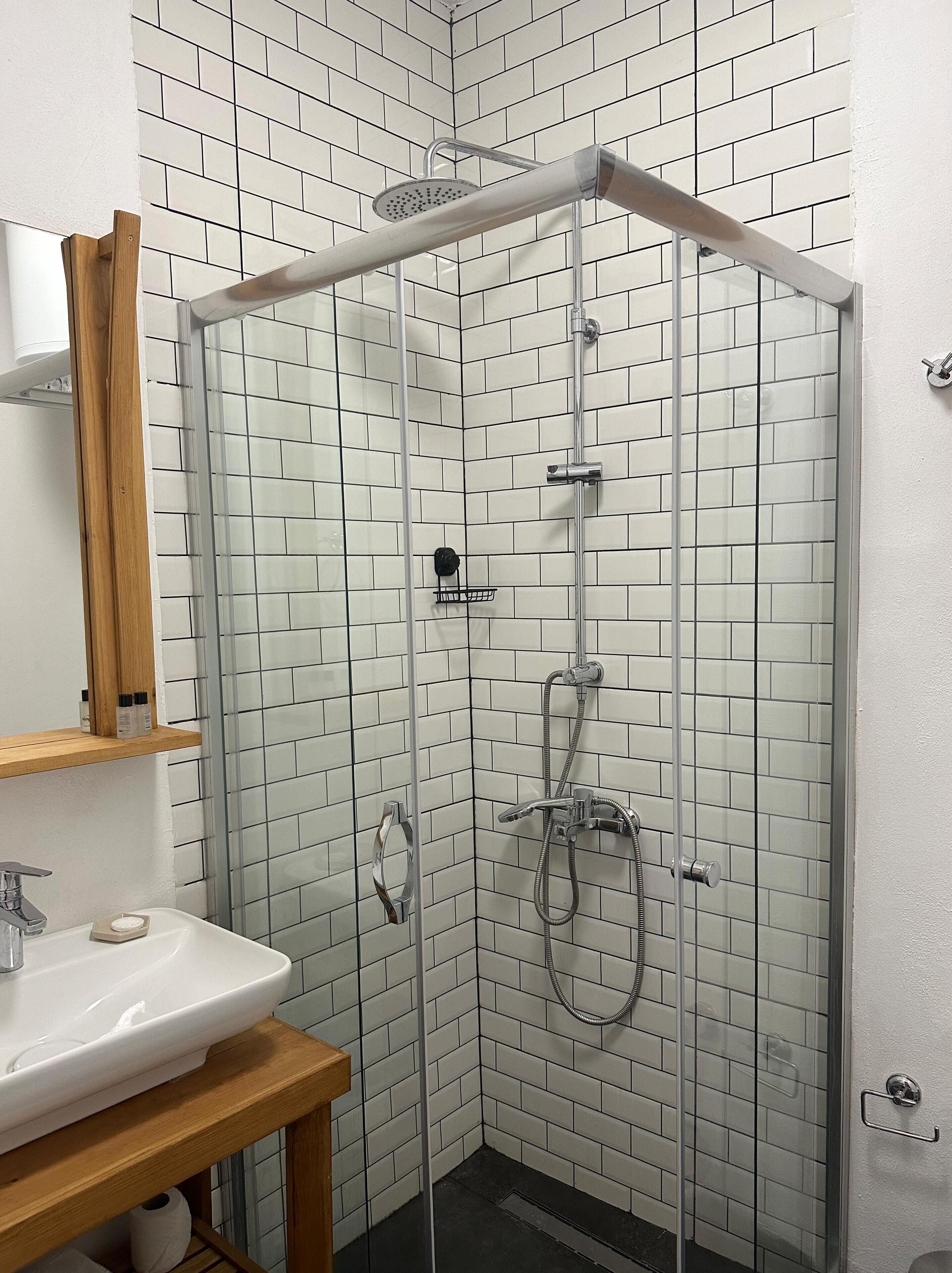 A modern bathroom with a glass-enclosed shower, white tiled walls, a wooden vanity with a sink, and a mirror.