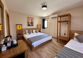 Habitación de hotel con una cama grande, una mesita de noche con hervidor y botella de agua, un banco de madera, aire acondicionado de pared y un cuadro.
