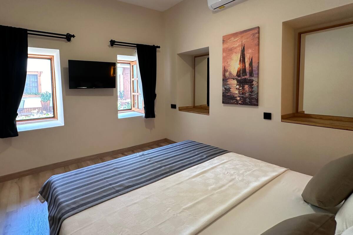 Un dormitorio con una cama, un televisor de pantalla plana, un cuadro y una ventana con cortinas.