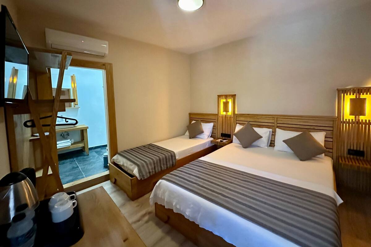 Habitación de hotel con dos camas individuales, un aparador de madera, un espejo, un televisor y una mesita pequeña con tazas y una tetera.