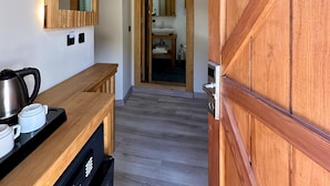 A hallway with a wooden bench, a coffee maker, and a mirror on the wall.