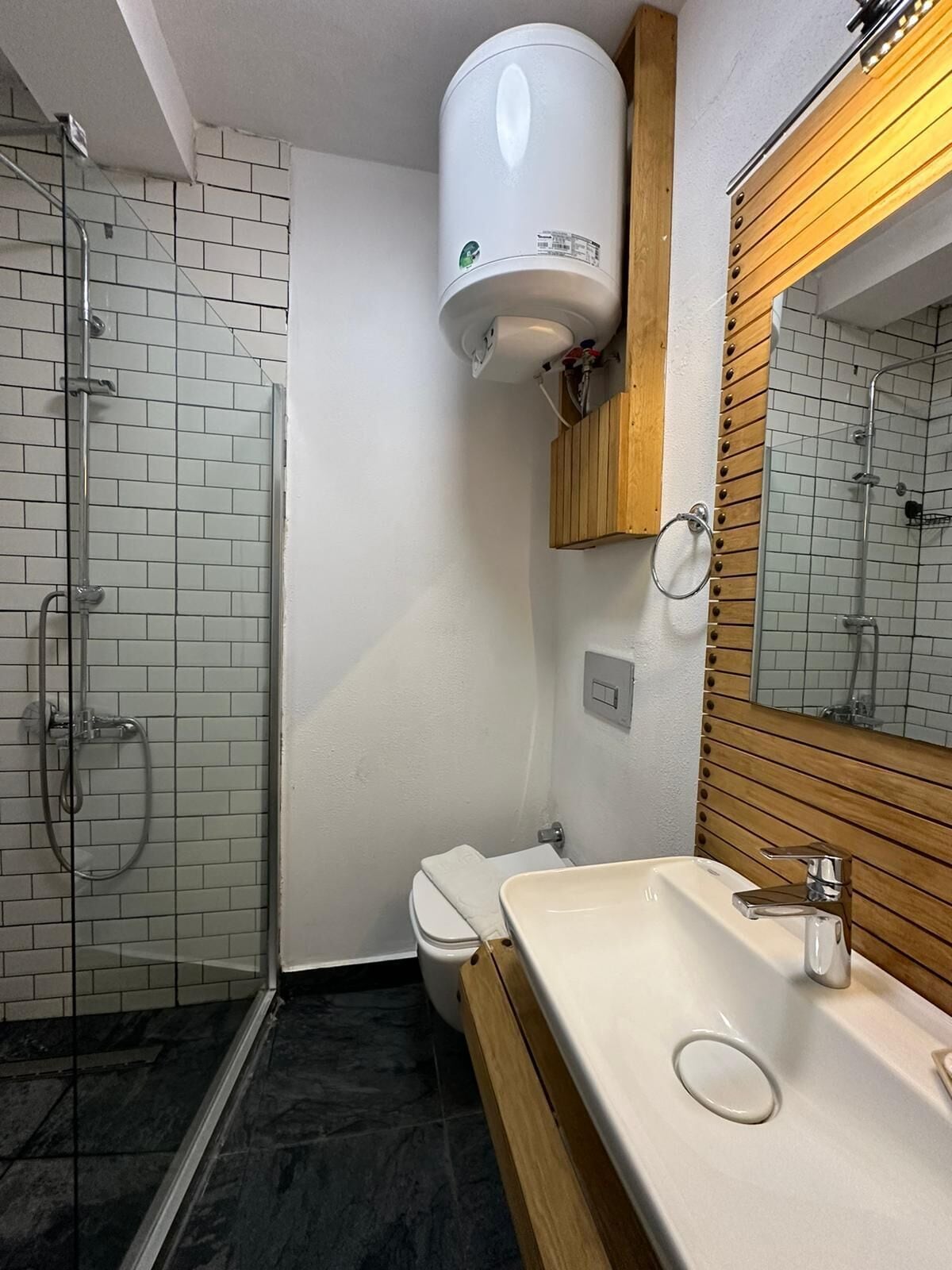 A bathroom with a glass shower enclosure, a toilet, and a sink with a wooden vanity.