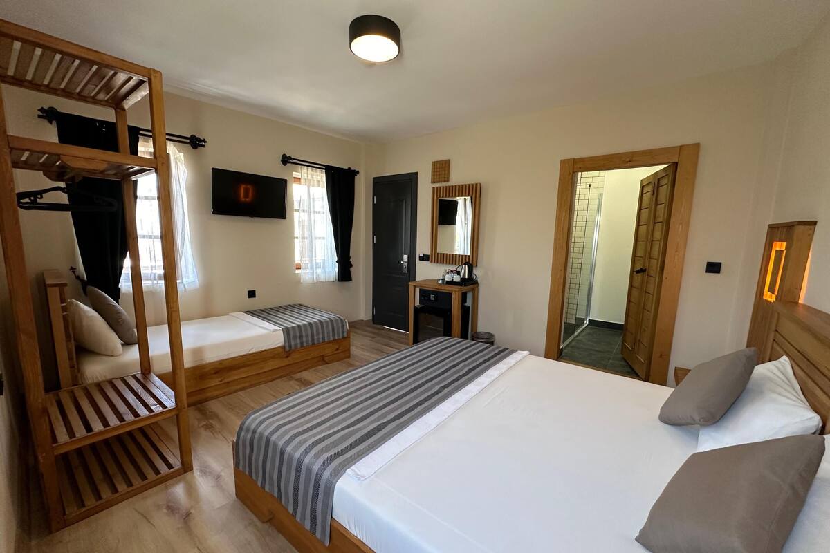 Habitación de hotel con una cama grande, una cama individual, una litera de madera, un escritorio, un espejo y zona de ducha.