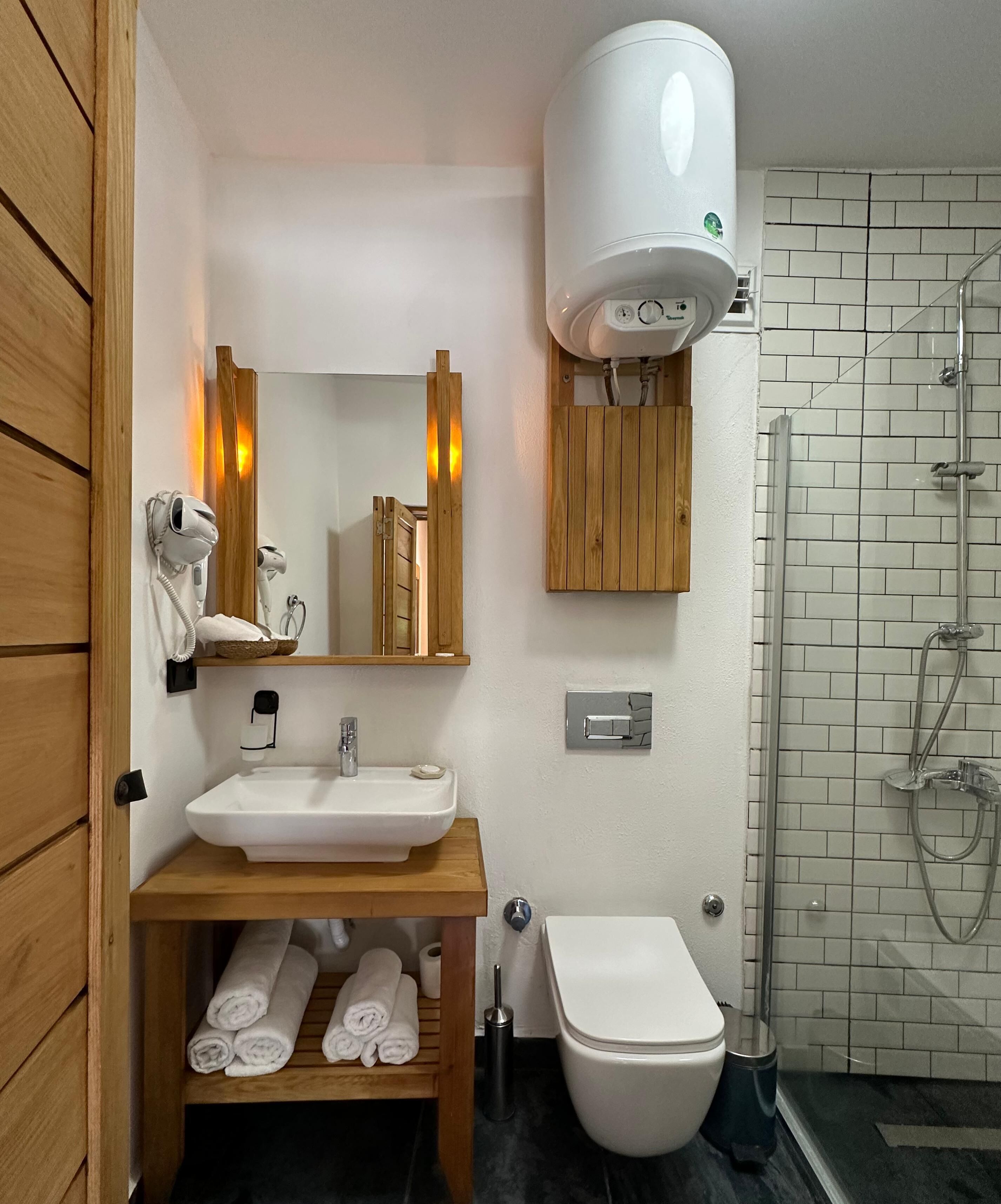 Ein Badezimmer mit einem Holzkosmetikschrank, einem weißen Waschbecken, einer Toilette, einer Dusche mit Glastür und einem Handtuchhalter mit Handtüchern.