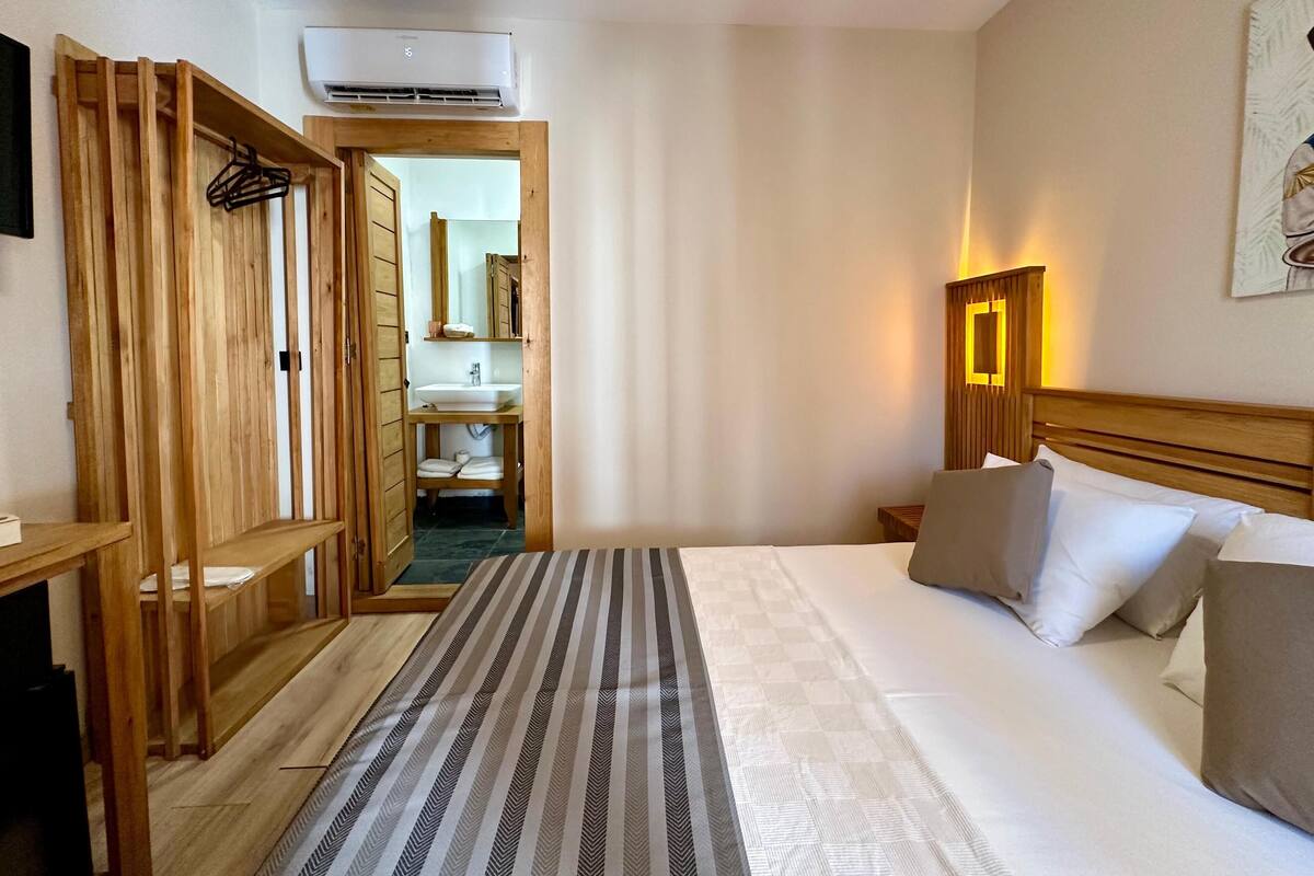 Una habitación de hotel con cama, mesita de noche, lámpara y un armario de madera.