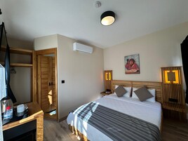 Habitación de hotel con cama, armario, escritorio con hervidor y botella de agua, aire acondicionado y un cuadro en la pared.