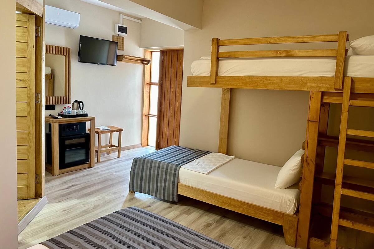 Una habitación con una cama litera, un escritorio con una computadora, un microondas y una pequeña mesa con tazas y una tetera.