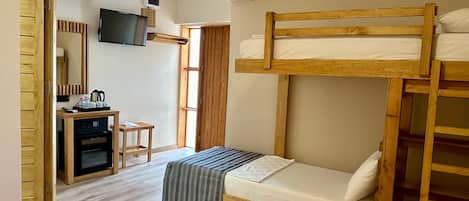 Una habitación con una cama litera, un escritorio con una computadora, un microondas y una pequeña mesa con tazas y una tetera.