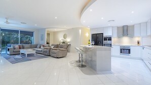 A modern open-plan living area with a sofa set, a dining bar, and a kitchen with white cabinetry and stainless steel appliances. - Walk to Golf Course, Lagoon Pool, Coastal Lux Home (Pelican Waters)
