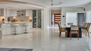 A modern kitchen with white cabinets, a central island with bar stools, and a dining area with a dark table and beige chairs. - Walk to Golf Course, Lagoon Pool, Coastal Lux Home (Pelican Waters)