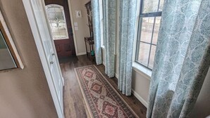 Um corredor com tapete estampado, porta de madeira e cortinas padronizadas.