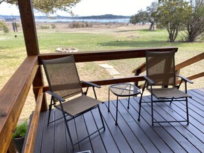 Eine Holzterrasse mit zwei Stühlen, die auf ein grünes Feld und ein Gewässer im Hintergrund blicken.