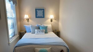 Quarto com cama, duas luminárias de cabeceira, janela com persianas e um quadro na parede.