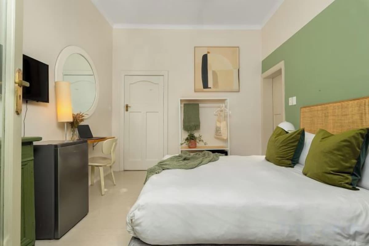 A bedroom with a bed, a desk, a chair, a television, and a door.