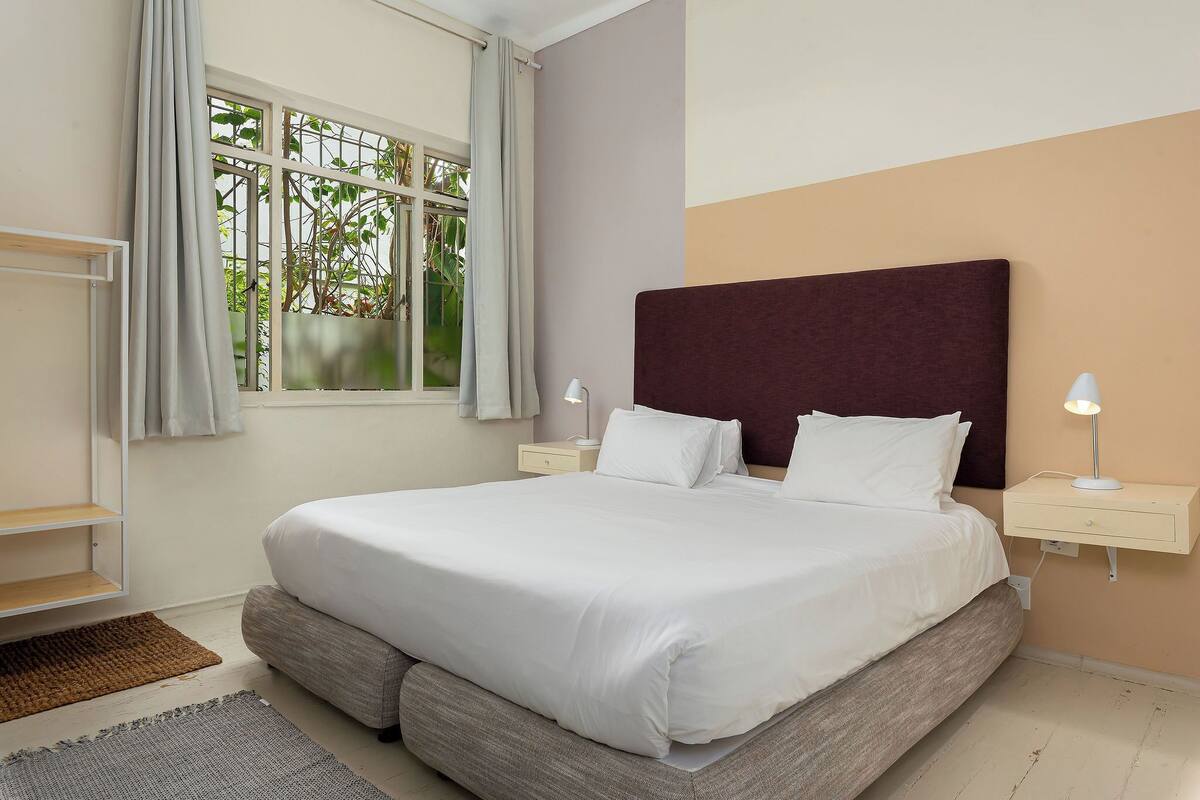 A neatly made bed with white linens, a dark headboard, and two bedside tables with lamps.
