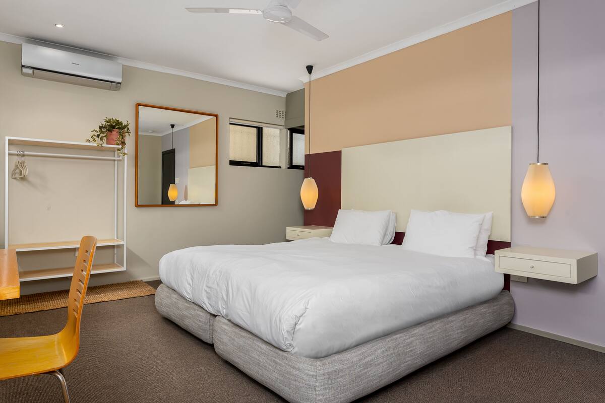 A hotel room with a large bed, a desk, a chair, a mirror, and a ceiling fan.