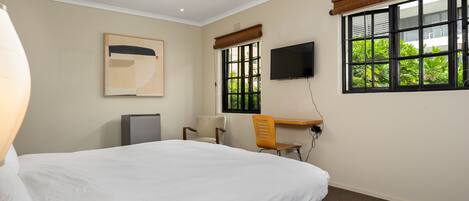 Habitación de hotel con cama, escritorio, silla, televisor y ventana con vista a zonas verdes.