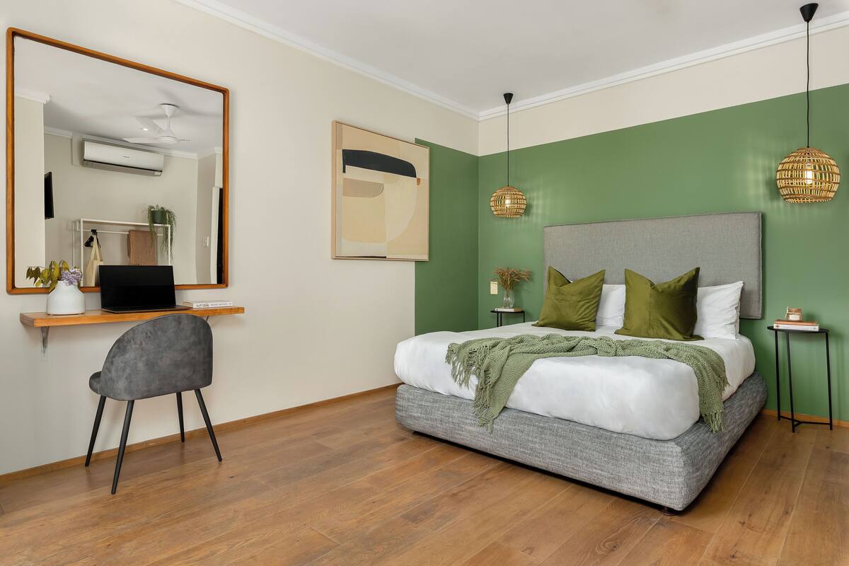 A bedroom with a bed, a desk, a chair, a mirror, and two pendant lights.