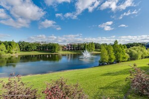 Een vredig landschap met een vijver, weelderige begroeiing en een gebouw op de achtergrond.