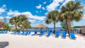 A beach with rows of blue lounge chairs, palm trees, and thatched umbrellas. - Bahama Bay - Minutes from Disney Theme Parks! (Davenport)