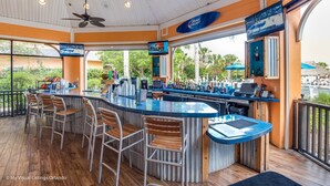 A bar area with a poolside view, bar stools, a ceiling fan, and a Bud Light sign. - Bahama Bay - Minutes from Disney Theme Parks! (Davenport)
