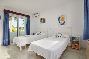 Une chambre d’hôtel avec deux lits, une petite table de chevet, un climatiseur fixé au mur et une fenêtre avec des rideaux bleus.