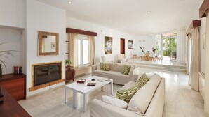 A spacious living room with a fireplace, a dining area with a view, and a large window. - Villa Punta des Port 13 by dracmallorca (Porto Petro)