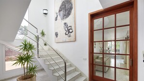 A staircase with a glass door, a potted plant, and a wall-mounted artwork. - Villa Punta des Port 13 by dracmallorca (Porto Petro)