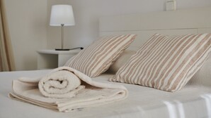 A neatly made bed with striped pillows and a rolled towel, a bedside lamp, and a small bedside table. - Villa Punta des Port 13 by dracmallorca (Porto Petro)