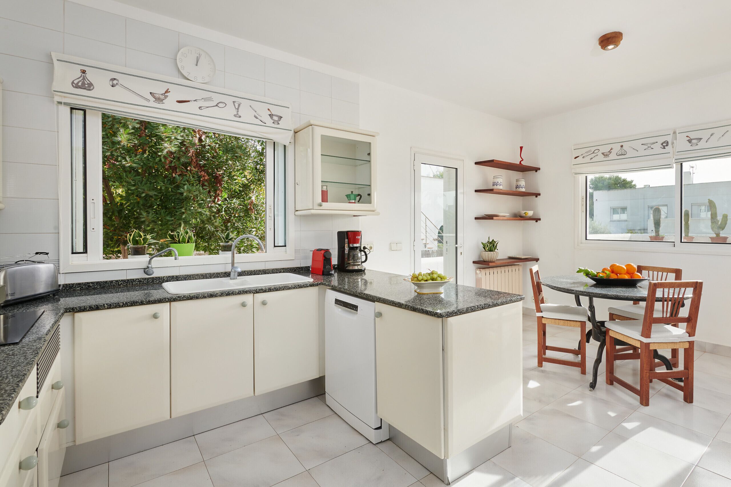 A modern kitchen with white cabinets, a dishwasher, a coffee maker, and a dining area with chairs and a table.