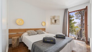 A hotel room with a wooden headboard, two beds with grey bedding, a small wooden stool, a wall clock, and a painting. - El Faro, frontline apartment with sea views, wifi (Puerto Pollensa)