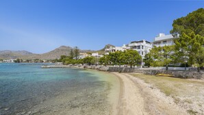 A coastal area with clear waters, sandy beach, and buildings with balconies overlooking the sea. - El Faro, frontline apartment with sea views, wifi (Puerto Pollensa)