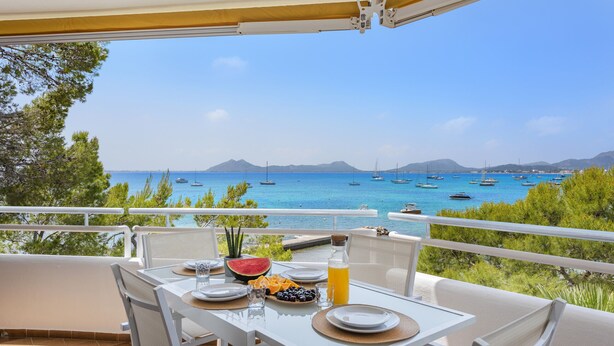 A terrace with a table set for breakfast, overlooking a sea with boats and mountains in the background. - El Faro, frontline apartment with sea views, wifi (Puerto Pollensa)