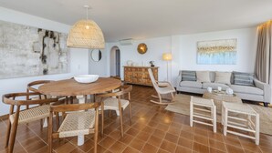 A modern living room with a round wooden dining table, wicker chairs, a sofa, and a large abstract painting. - El Faro, frontline apartment with sea views, wifi (Puerto Pollensa)