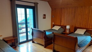 Une chambre avec deux lits en bois, une petite table et une porte-fenêtre coulissante donnant sur un espace extérieur.