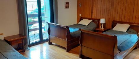 A room with two wooden beds, a small table, and a sliding glass door leading to an outdoor area.
