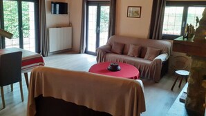 Une pièce confortable avec un canapé, une table et une chaise. Il y a un téléviseur accroché au mur et une fenêtre avec des rideaux.