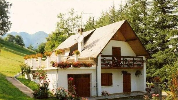 Une maison blanche avec un toit en pente, un balcon en bois et un petit porche.