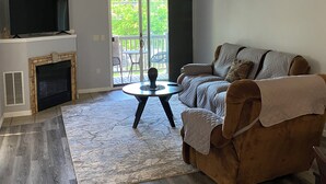 Un salon avec une cheminée, un canapé, un téléviseur et une vue sur l’extérieur.