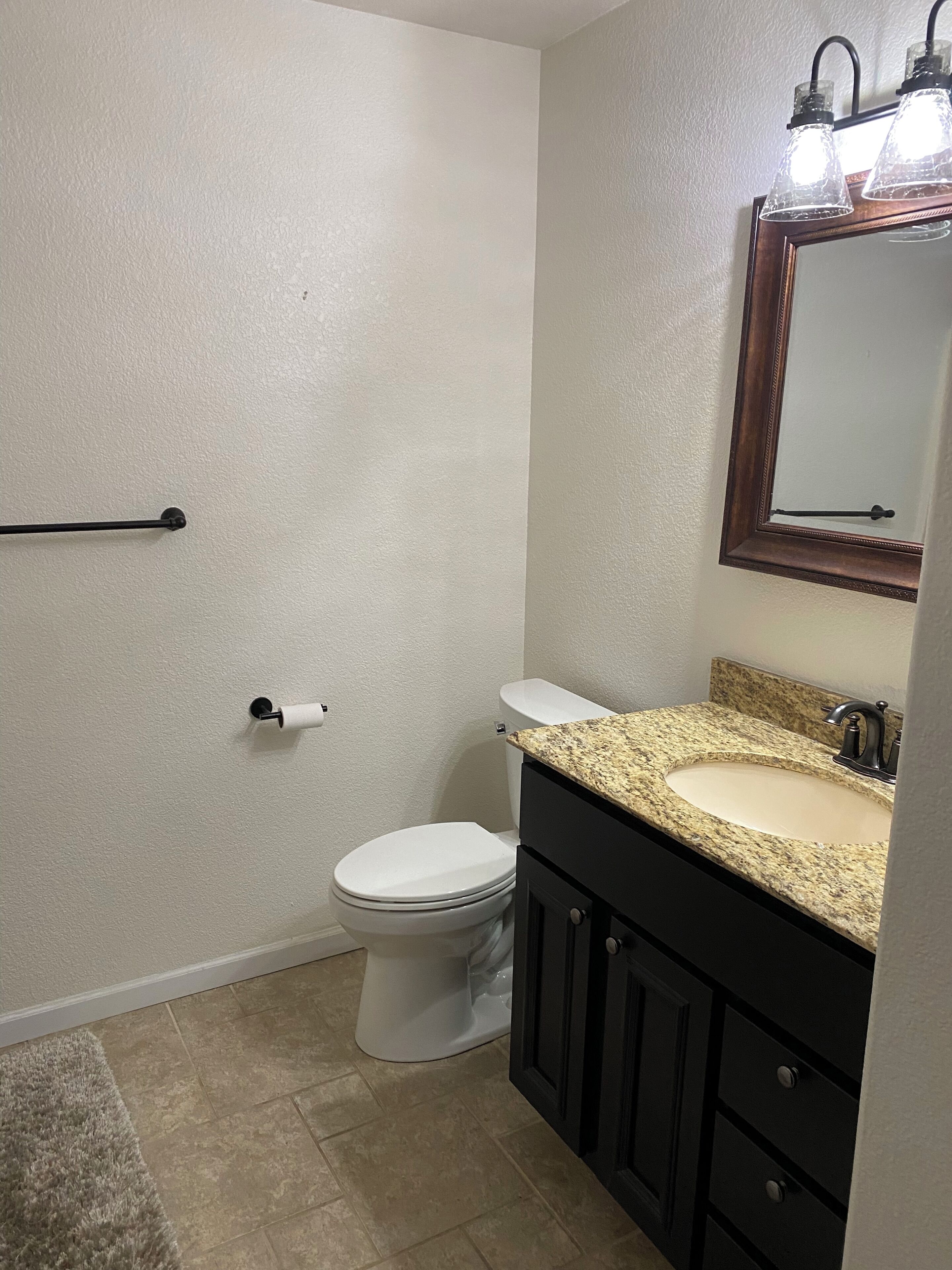 A bathroom with a toilet, sink, vanity, and a mirror with lights.
