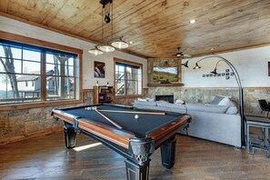 A pool table in a room with wooden ceilings, a stone wall, and a large window.