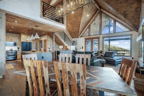 A spacious living area with a high ceiling, wooden beams, and a large window offering a view of the outdoors.