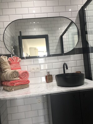 Une salle de bain avec un mur recouvert de carreaux blancs, un lavabo noir et un miroir à cadre noir.