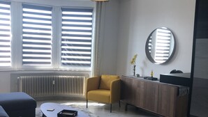 Un saló modern amb un sofà, una taula de centre, un butàquic groc, un mirall rodó i un armari.
