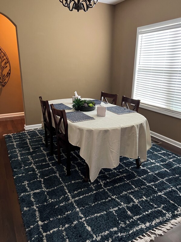 Un coin repas avec une table ronde, quatre chaises, une nappe blanche, un centre de table agrémenté de plantes et un tapis à motifs bleus.